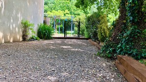 A gravel pathway leading to a fenced area with a view of a lush garden and a building on the left.