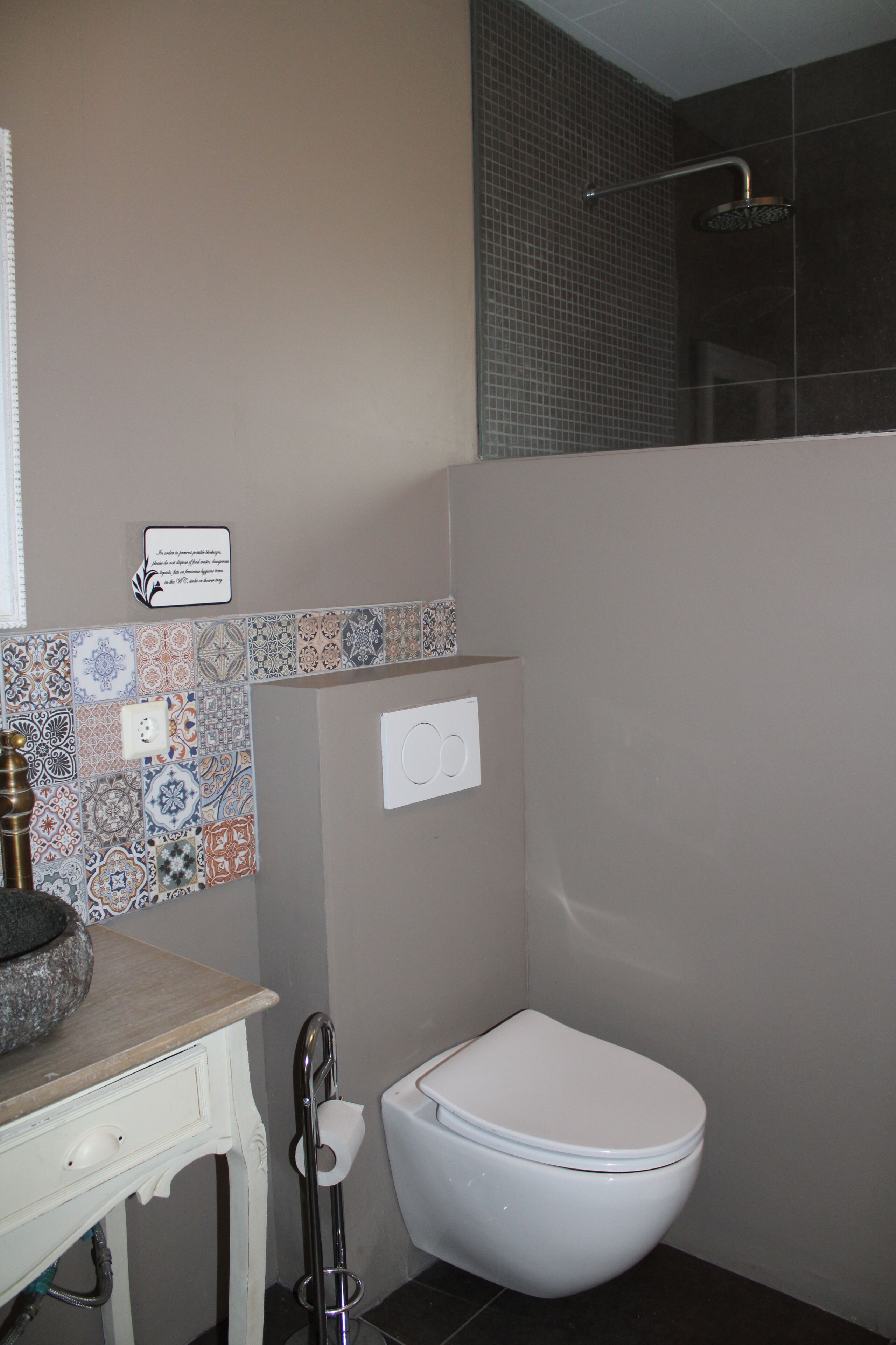 A bathroom with a toilet, a sink, and a shower. There is a decorative tile backsplash above the sink and a showerhead above the shower.