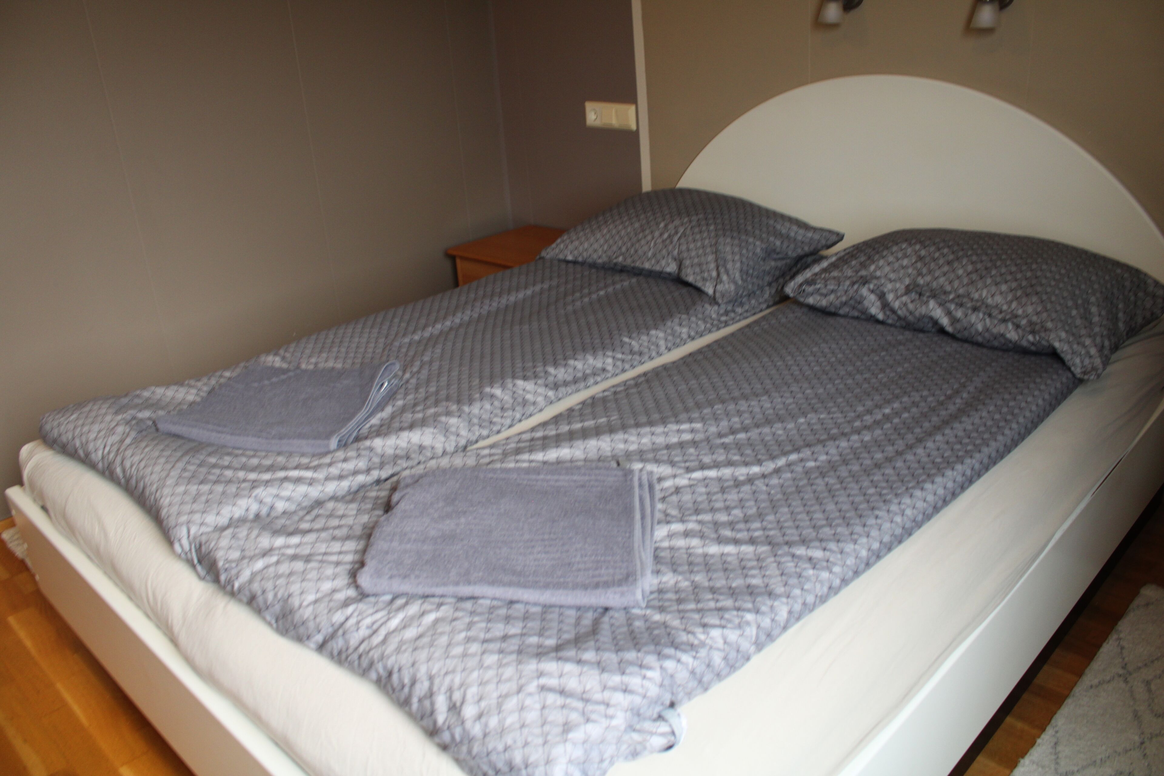 A single bed with a white headboard and grey bedding.