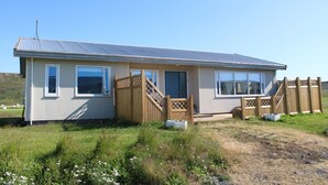A single-story house with a metal roof, a wooden deck, and a small front porch. - Stóri-Bakki Guesthouse with hot tub (Egilsstaðir)