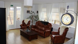 A living room with leather furniture, a clock, and a view of the outside. - Stóri-Bakki Guesthouse with hot tub (Egilsstaðir)