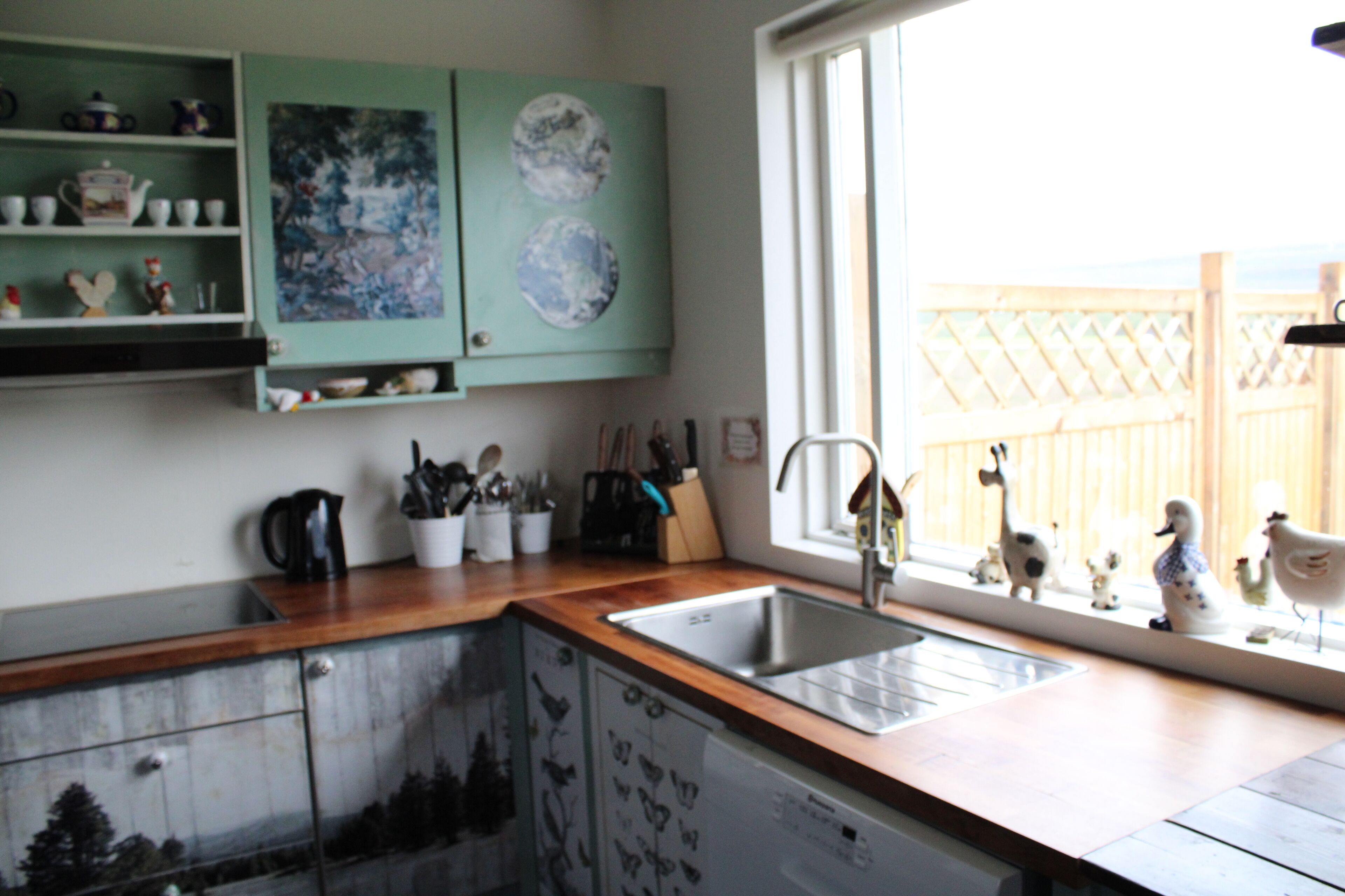 A kitchen with a wooden countertop, a stainless steel sink, and a window with a view of a wooden fence.