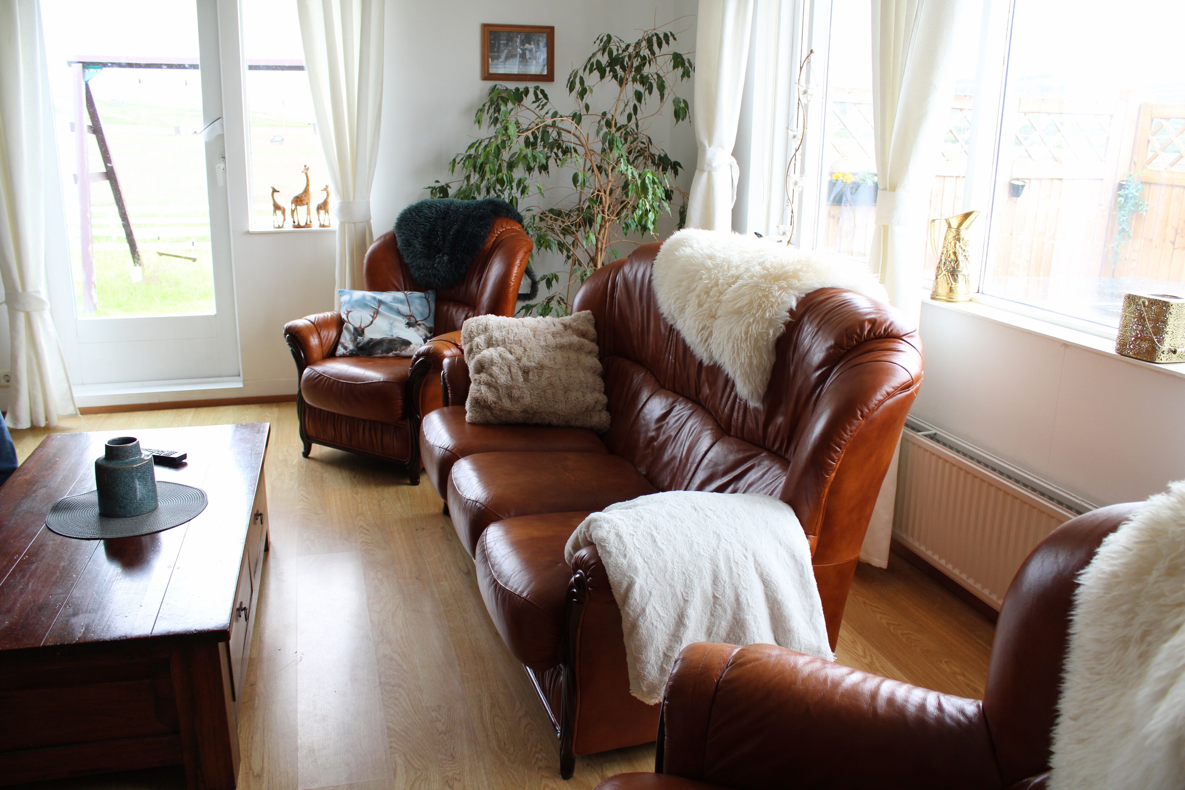 Una sala de estar con un sofá de cuero marrón, una mesa de centro de madera y un ventanal con cortinas.