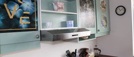 A kitchen with teal cabinets, a stainless steel range hood, and various kitchen items on the counter.