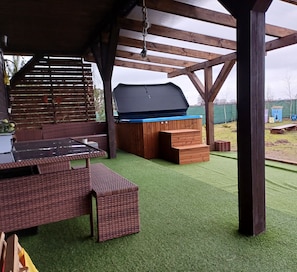 An outdoor patio with a grill, wooden furniture, and artificial turf. - dom wakacyjny z sauną i jacuzzi 153 m ,3 sypialnie ,10 mni do plaży (Skulsk)