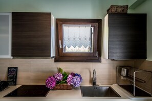 A kitchen with wooden cabinets, a window with lace curtains, a sink, and a basket of flowers.