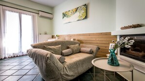 A living room with a sofa, a small round table, a vase with flowers, a fireplace, and a painting on the wall. - Daphne House In Pelion (Zagora-Mouresi)
