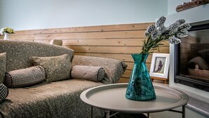 A living room with a patterned sofa, a teal vase with flowers, and a framed picture on a small table. - Daphne House In Pelion (Zagora-Mouresi)