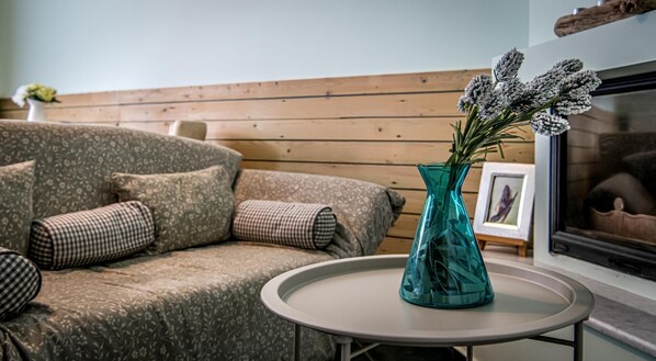 A living room with a patterned sofa, a teal vase with flowers, and a framed picture on a small table.