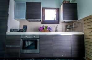 A modern kitchen with dark wood cabinets, a built-in oven, a window above the sink, and a basket of flowers on the counter.