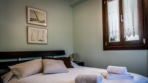 A neatly made bed with pillows and folded towels, a bedside table with a lamp, and two framed artworks on the wall. - Daphne House In Pelion (Zagora-Mouresi)