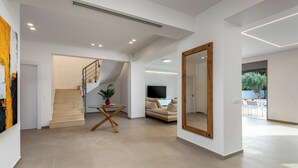 A spacious living area with a staircase, a flat-screen TV, a large mirror, and a dining area with a table and chairs. - Ialysos Charme Villa (RHODES)