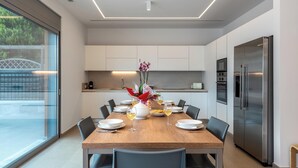 A modern kitchen with a dining table set for six, a large refrigerator, and a view through a glass door. - Ialysos Charme Villa (RHODES)