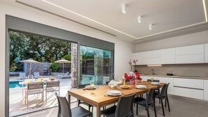 A modern kitchen with white cabinets and a dining area with a wooden table and chairs. - Ialysos Charme Villa (RHODES)