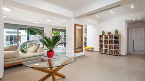 A modern living room with a glass-top coffee table, a sofa, a potted plant, and a bookshelf. - Ialysos Charme Villa (RHODES)