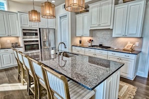 A kitchen with white cabinets, a granite island, bar stools, and pendant lighting.