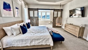 Une chambre avec un grand lit, une télévision, un fauteuil en rotin et une vue sur l’extérieur.