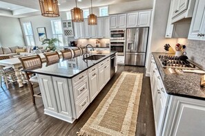 A modern kitchen with white cabinetry, a central island, stainless steel appliances, and a dining area with a wooden table and chairs.