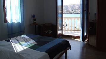 Un dormitorio con cama, una mesita y una silla. Cuenta con un balcón con vistas al mar y a las montañas.