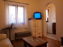 Una stanza piccola e accogliente con un letto, una scrivania con un computer portatile, una televisione su un mobile e un angolo cottura sullo sfondo.