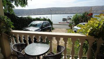 A balcony with a table and chairs, overlooking a body of water with boats and a distant cityscape.