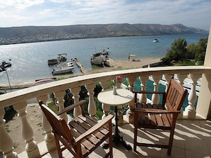 A balcony with two wooden chairs and a small table, overlooking a marina with boats and a beach. - Pansion Gea (Pag)