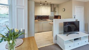 Una cocina moderna con armarios blancos, horno empotrado y comedor con mesa de madera y un florero.