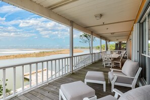 A covered outdoor area with a wooden deck, white cushioned chairs, and a view of a river and distant landscape.