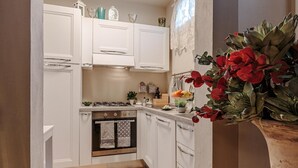 A kitchen with white cabinets, a stove, oven, and a sink. There is a decorative plant with red flowers on the counter. - Casa Uccellini in Lucca (Lucca)