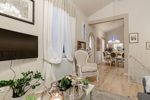 Uma sala de estar com televisão de tela plana, um espaço de refeições com lustre e uma escada.
