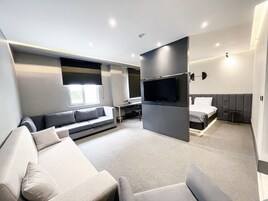 A modern hotel room with a sofa, a bed, a TV, and a desk.