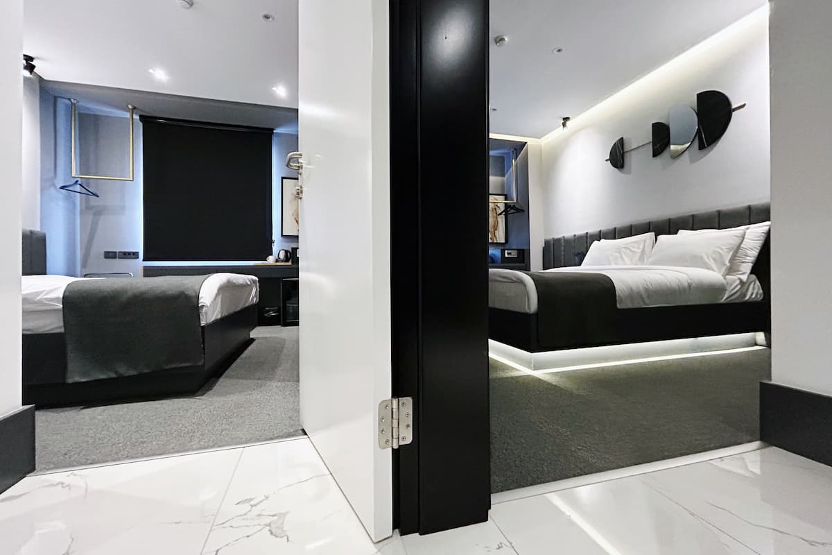 A modern hotel room with a large bed, a smaller bed, a desk, and a seating area.