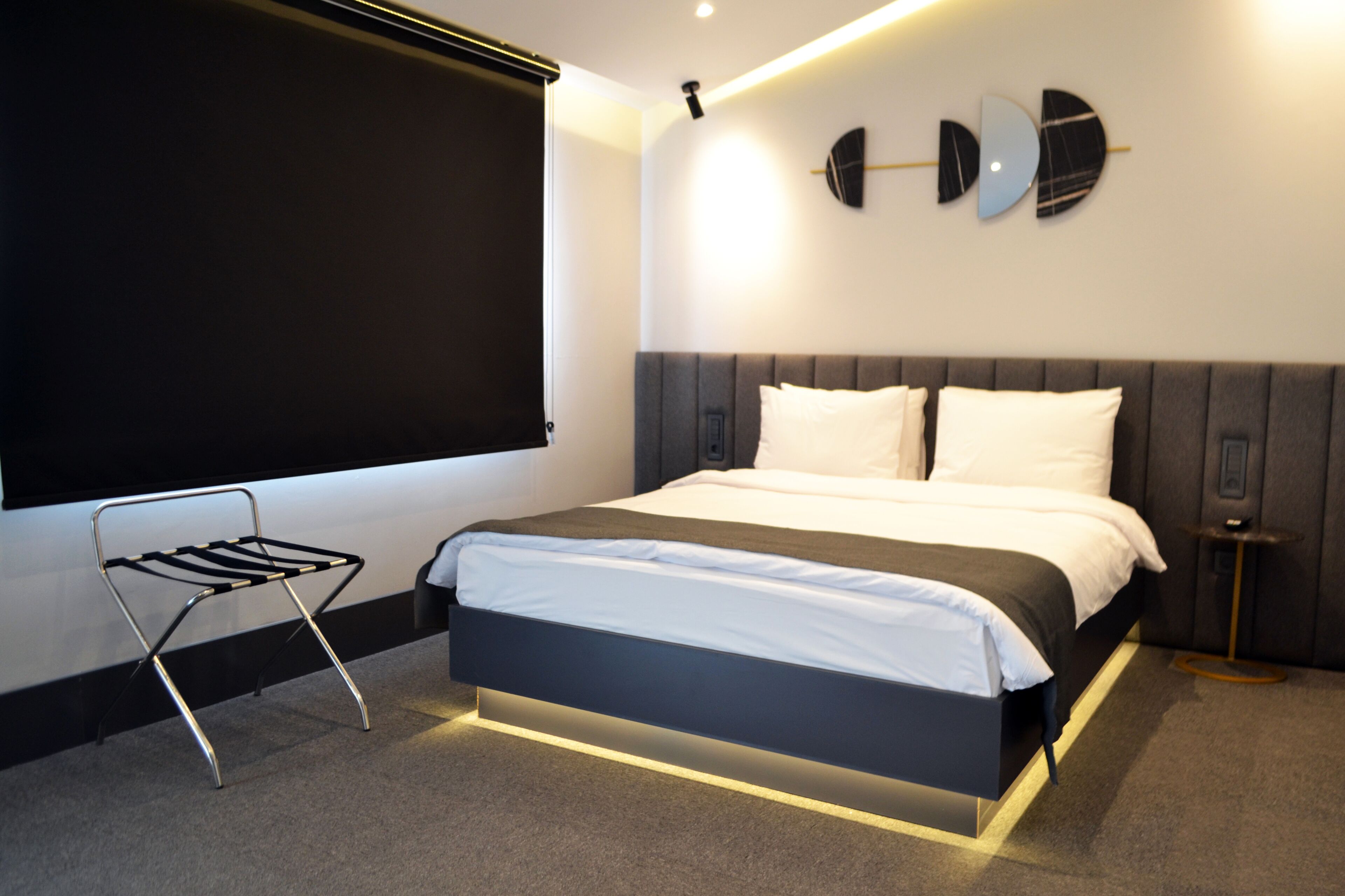 Una habitación de hotel moderna con una cama grande, una mesita auxiliar pequeña, una silla y una pantalla proyectora instalada en la pared.