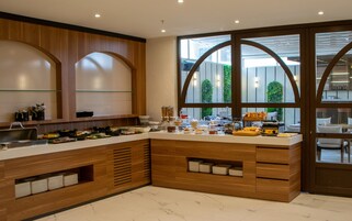 A modern kitchen with a marble countertop, wooden cabinets, and a view of greenery through large windows.