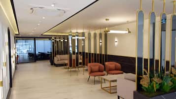 Un hall d’hôtel moderne avec un sol en marbre, un espace salon doté de canapés et de fauteuils, un comptoir d’accueil et des miroirs décoratifs.