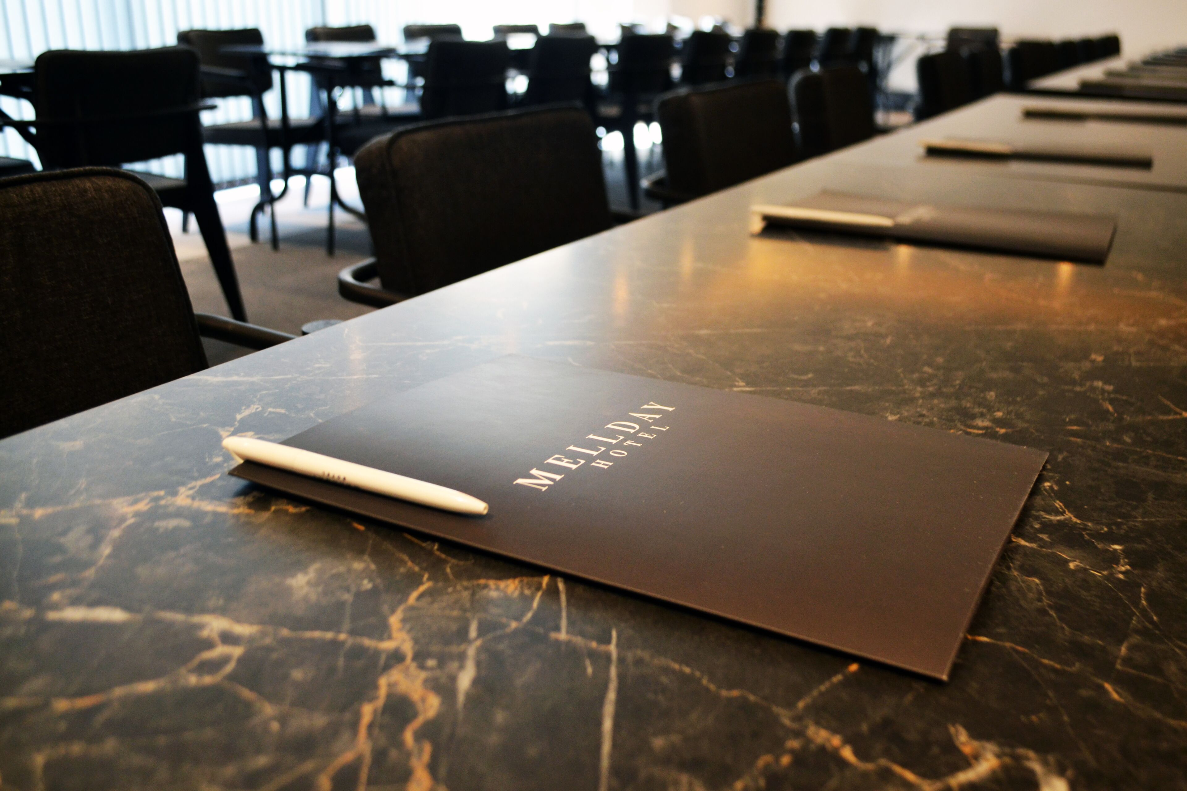 A conference table with a folder labeled "MELDAY HOTEL" and a pen on it.