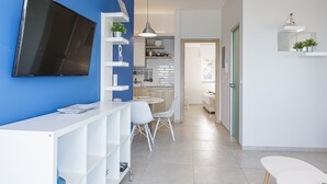 Una cocina moderna con armarios blancos, un área de comedor con mesa y sillas blancas, y un televisor montado en la pared.