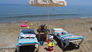 Una playa con dos tumbonas, una sombrilla y una pequeña mesa con un sombrero y gafas de sol.