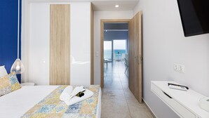 Habitación de hotel con cama, televisión, escritorio y vista al mar a través de una puerta abierta.