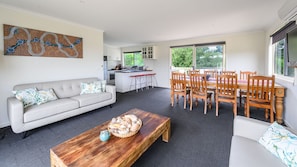 A modern living room with a sofa, wooden coffee table, and a dining area with chairs and a table. - Pleiades, Venus Bay (pet friendly) (Venus Bay)