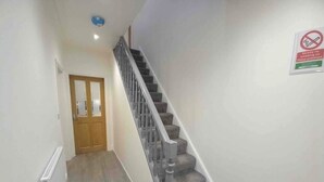 Un escalier avec une rampe, des marches recouvertes de moquette et une porte en bas.