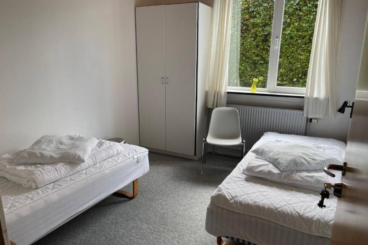 A bedroom with two beds, a wardrobe, a radiator, and a window with curtains.