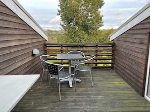 A wooden deck with a table and chairs, surrounded by wooden walls and a view of trees.