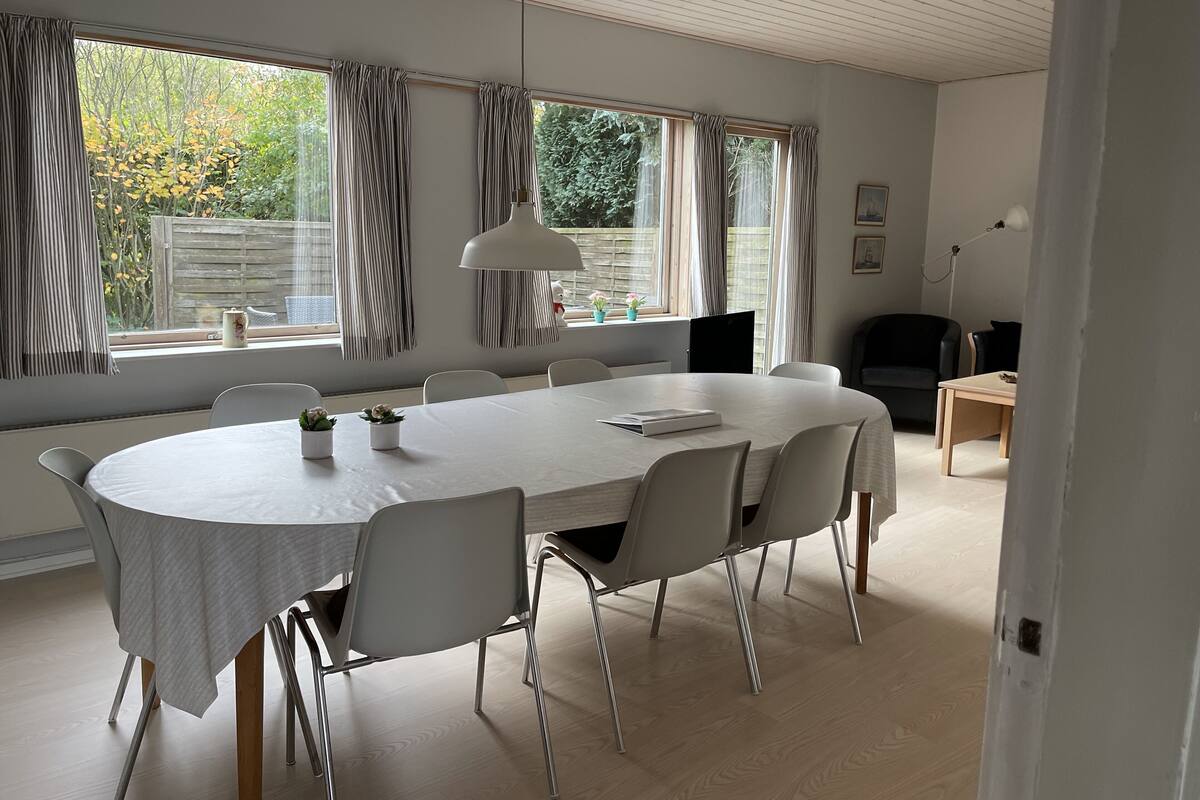 A modern dining room with a large oval table, white chairs, and a white pendant light.