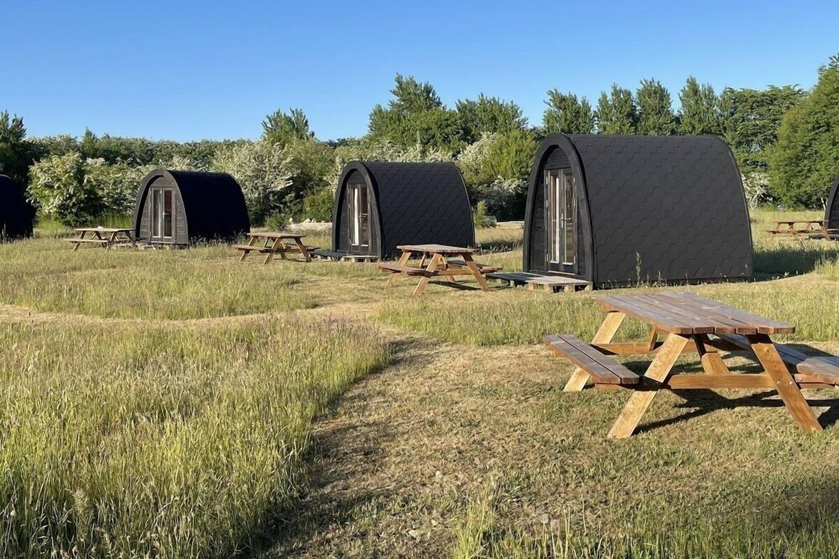 A row of geodesic dome-style cabins with picnic tables in a grassy field.