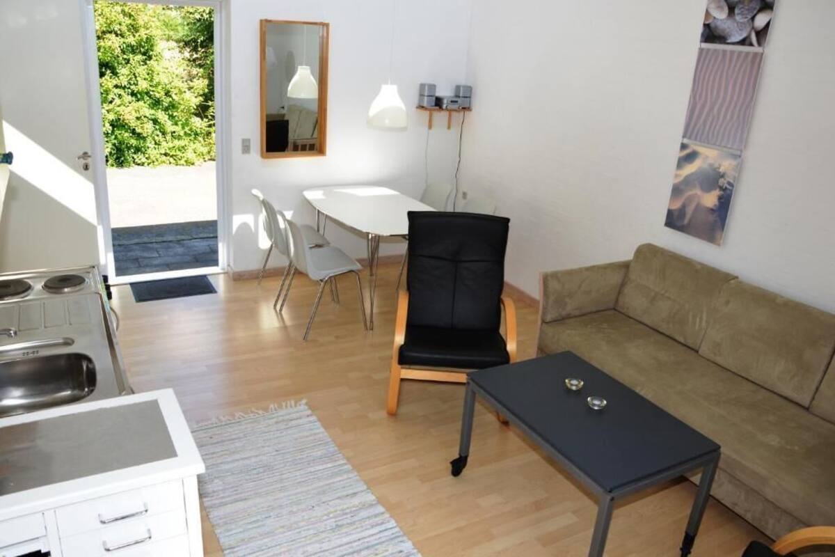 A compact living space with a kitchenette, a dining area with chairs, a black chair, a sofa, and a small table.