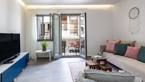 En moderne stue med et fladskærms-tv, en sofa med puder, et sofabord og en skydedør til en balkon.