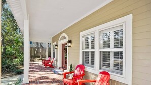 A covered porch with red Adirondack chairs, a brick floor, and a beige exterior wall with white trim. - Beach House, Pool, Golf Cart, Game Room, BBQ, (St. Augustine)