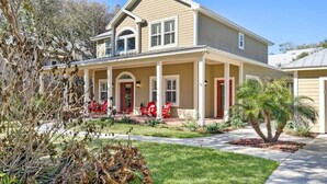 A two-story house with a covered porch, a front door, and a small garden with a palm tree. - Beach House, Pool, Golf Cart, Game Room, BBQ, (St. Augustine)