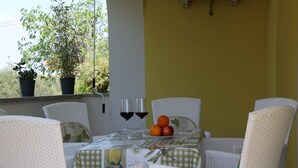 A table set with two wine glasses and a fruit bowl, surrounded by wicker chairs, with a view of greenery outside. - Apartment Marina (Punat)